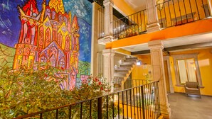 Un interior de hotel muy iluminado con un mural colorido de un castillo, una escalera y un balcón con una silla.