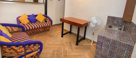 A compact living space with a sofa, a small table, a fan, and a sink.