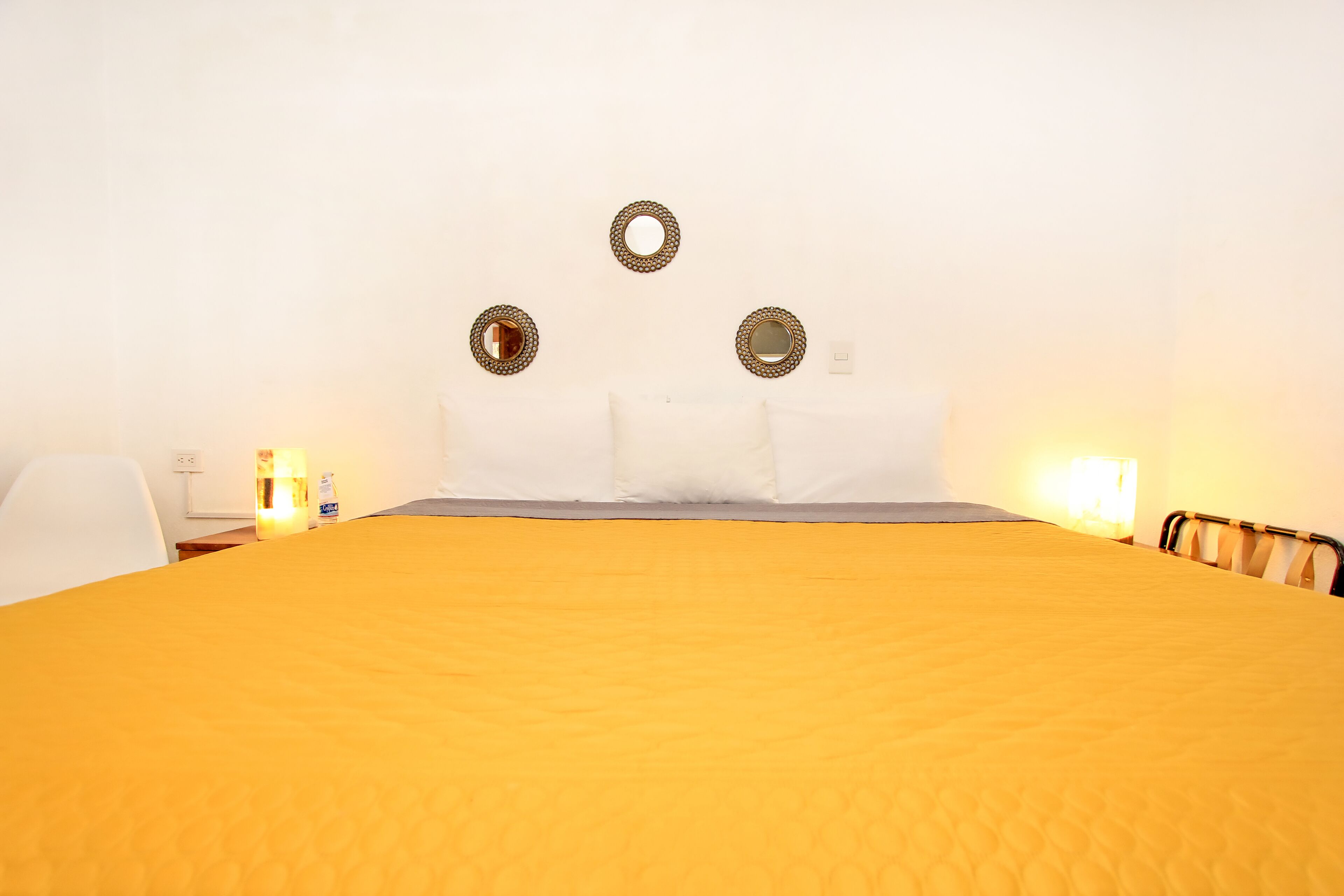 A room with a large bed, a white chair, and a nightstand with a lamp.