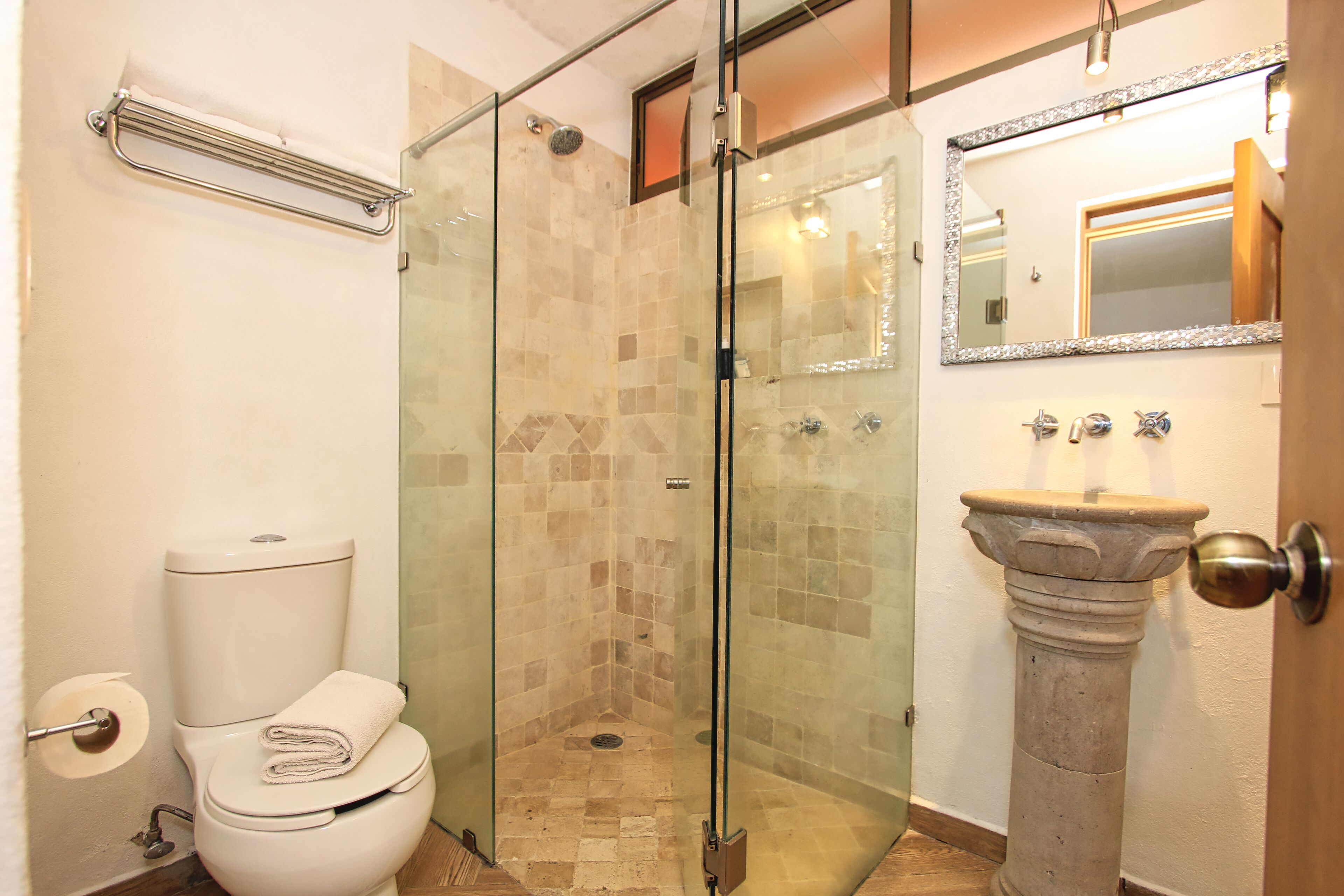 Un baño con cabina de ducha de vidrio, lavamanos pedestal y retrete.
