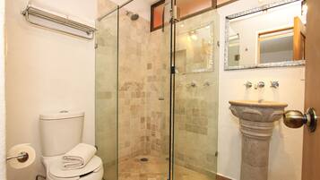 Un baño con cabina de ducha de vidrio, lavamanos pedestal y retrete.