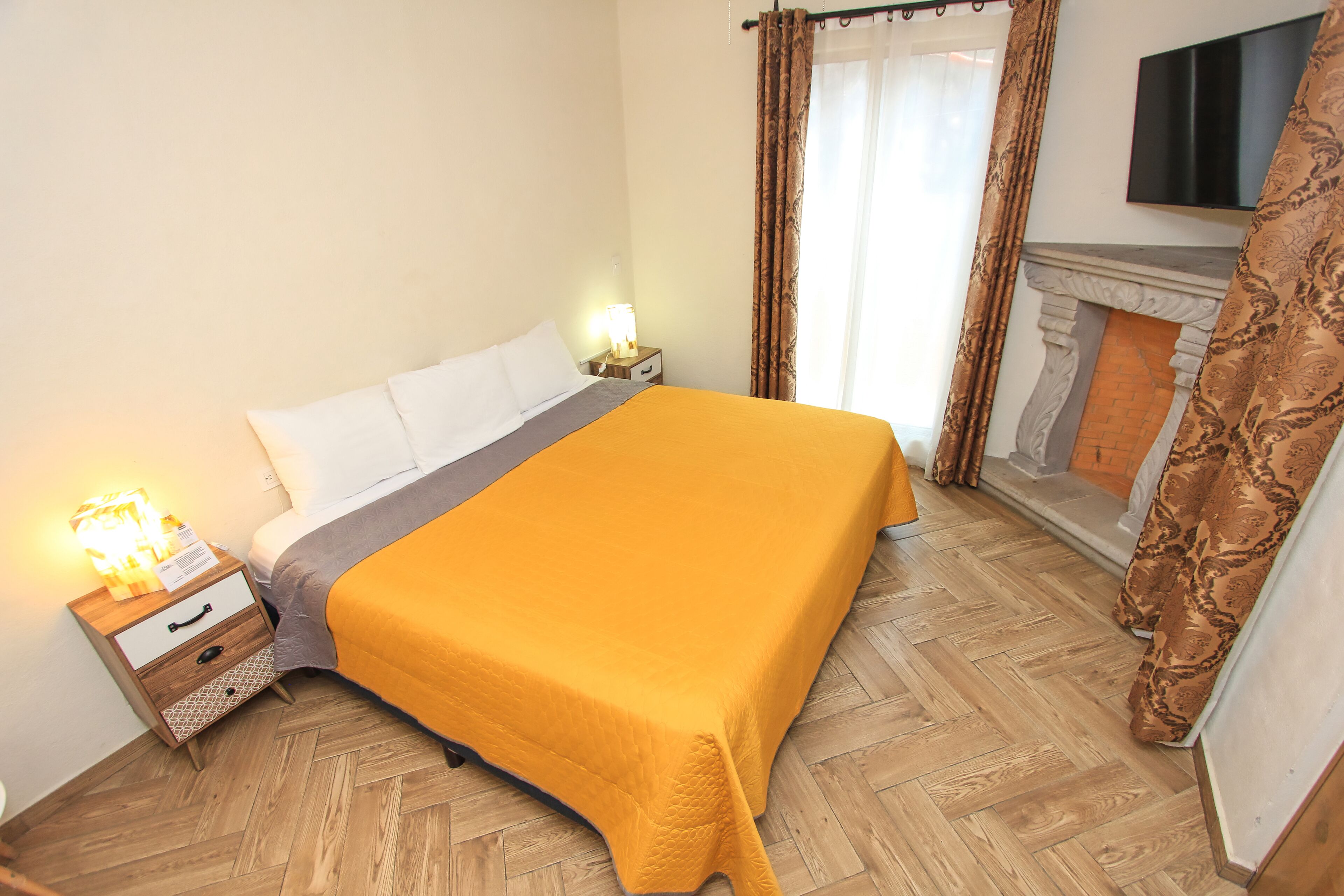 A hotel room with a bed, a nightstand, a TV, and a fireplace.
