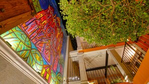 Una vidriera vibrante con diseños geométricos, una puerta de madera y un balcón con barandilla metálica y vegetación.
