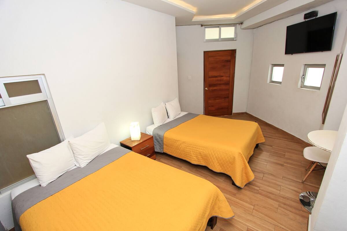 A hotel room with two beds, a TV, a wooden door, and a small table.