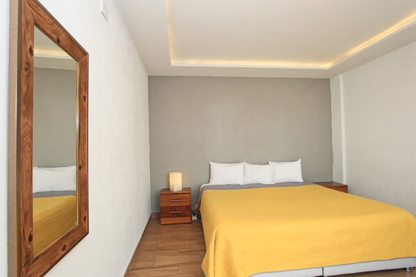 Un dormitorio con cama, mesita de noche, espejo y una lámpara en la mesita junto a la cama.