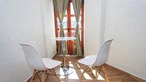 A corner room with two white chairs, a round table, and a view through a window with curtains.