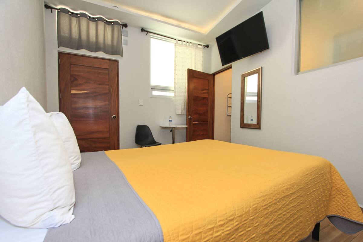 A bedroom with a bed, a TV mounted on the wall, and a window with curtains.