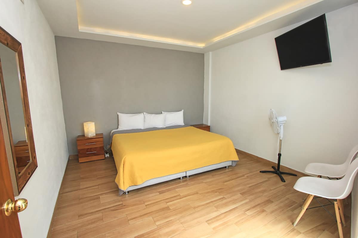 A bedroom with a bed, bedside table, lamp, chair, and a mounted TV.