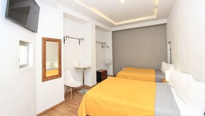A hotel room with two beds, a TV mounted on the wall, a small desk with a chair, and a mirror.
