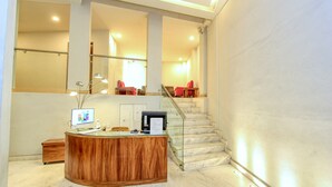 A reception desk with a computer, a small wooden cabinet, and a glass railing beside a staircase.