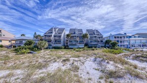 A beachfront hotel with multiple balconies, a sandy foreground, and clear skies. - Pelicans Pointe (Indian Shores)