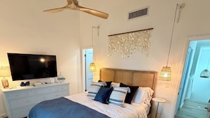 A modern bedroom with a large bed, a ceiling fan, a TV, and a decorative wall piece. - Pelicans Pointe (Indian Shores)