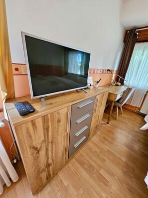 A wooden desk with a flat-screen TV, a remote control, and a small potted plant.