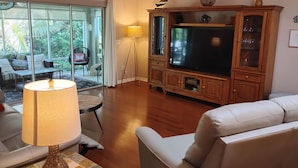 A living room with a large TV, wooden entertainment unit, and a ceiling fan. - Palm Paradise  - Great Location with a Courtesy Golf Cart (The Villages)