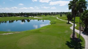 A golf course with a pond, palm trees, and a clear sky. - Palm Paradise  - Great Location with a Courtesy Golf Cart (The Villages)