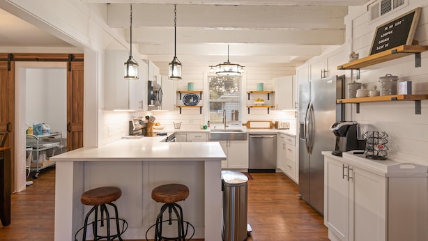 Une cuisine moderne dotée d’un îlot central, de tabourets de bar, d’appareils électroménagers en acier inoxydable et d’éléments décoratifs en bois.