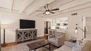 Un salon avec un ventilateur de plafond, un téléviseur, un canapé, une table basse et un meuble.