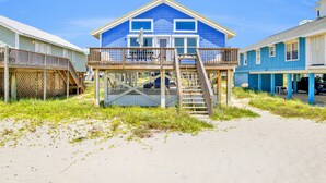 A beachfront house with a balcony, wooden deck, and a staircase leading to the upper floor.