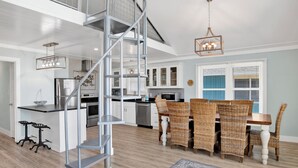 A modern kitchen with a central island, stainless steel appliances, and a dining area with wicker chairs and a wooden table.