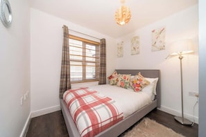 A bedroom with a bed, a window with curtains, a floor lamp, and wall art. - Stylish Hull Apt - City Centre & Gated Parking (Hull)