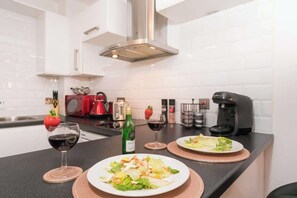 A modern kitchen with white cabinets, a stainless steel range hood, a coffee maker, and two plates of food on the counter. - Stylish Hull Apt - City Centre & Gated Parking (Hull)