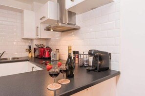 A modern kitchen with white cabinets, a stainless steel range hood, a coffee maker, a toaster, and two glasses of red wine on the counter. - Stylish Hull Apt - City Centre & Gated Parking (Hull)
