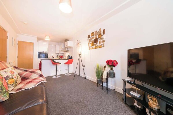 A compact living space with a sofa, a television, a kitchen area, and a dining table. - Stylish Hull Apt - City Centre & Gated Parking (Hull)
