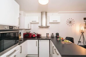 Une cuisine moderne avec des meubles blancs, une hotte en acier inoxydable et un plan de travail noir.