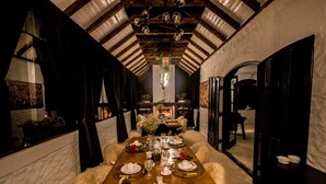 Ein Esszimmer mit einem Holztisch, gedeckt für eine Mahlzeit, mit weißen Zirbensofa-Polstern, einem Kronleuchter und einem Kamin im Hintergrund.