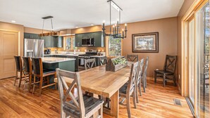 A modern kitchen with a central island, wooden dining table, and chairs. - Luxe Home with Hot Tub & Mountain Views (Estes Park)