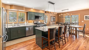 A modern kitchen with dark green cabinets, stainless steel appliances, and a large island with bar stools. - Luxe Home with Hot Tub & Mountain Views (Estes Park)