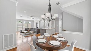 Un coin repas avec une table ronde dressée pour six personnes, entourée de chaises blanches.