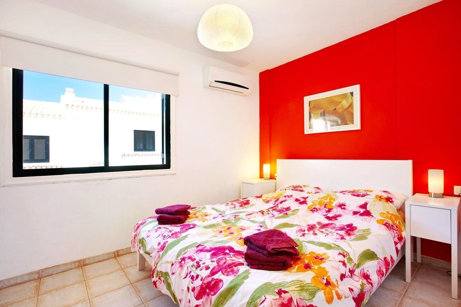 Un dormitorio con cama, mesita de noche, ventana y pared roja.
