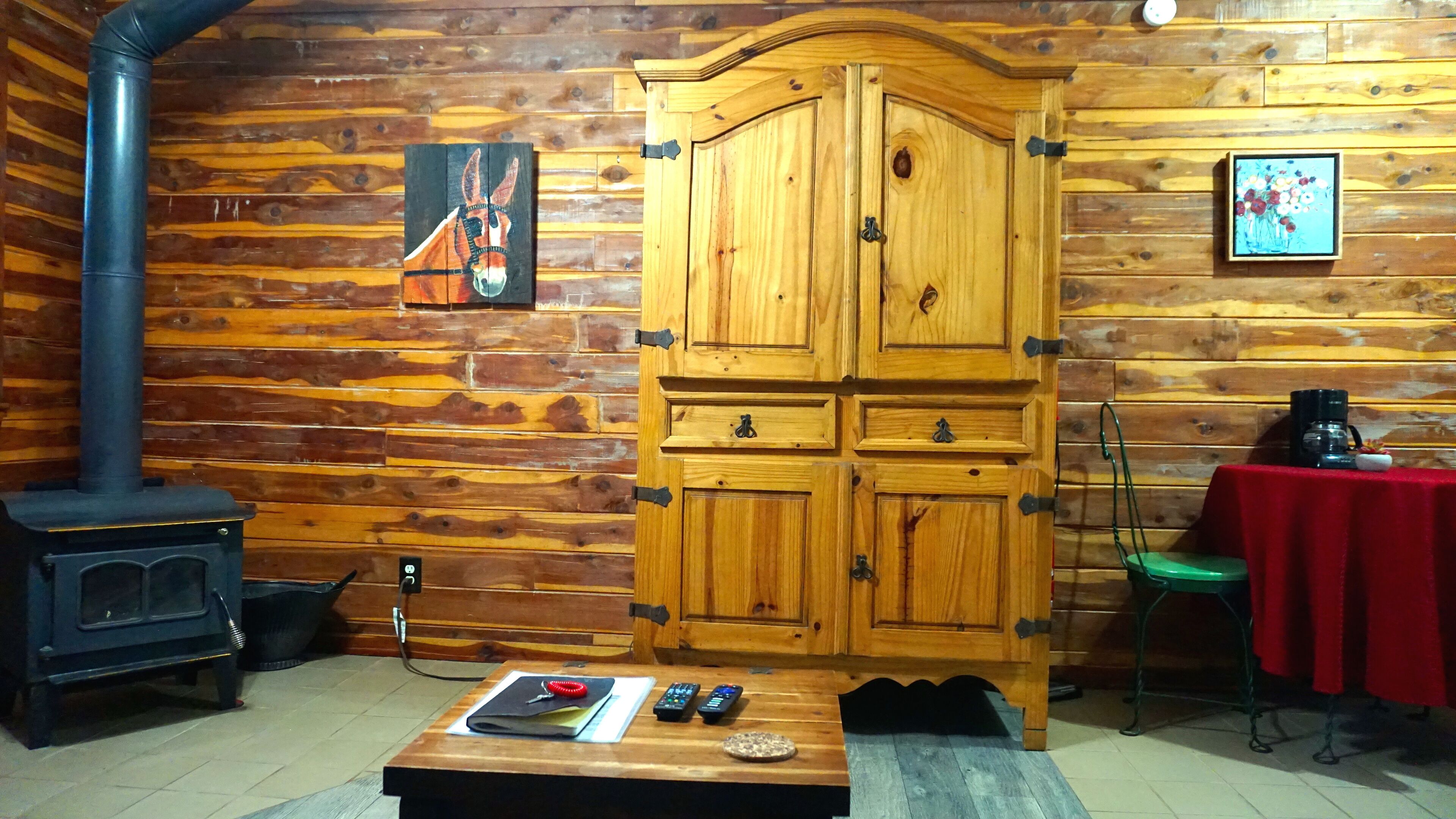 Interior de una cabaña de madera con un armario grande, una chimenea y una mesa con controles remotos.