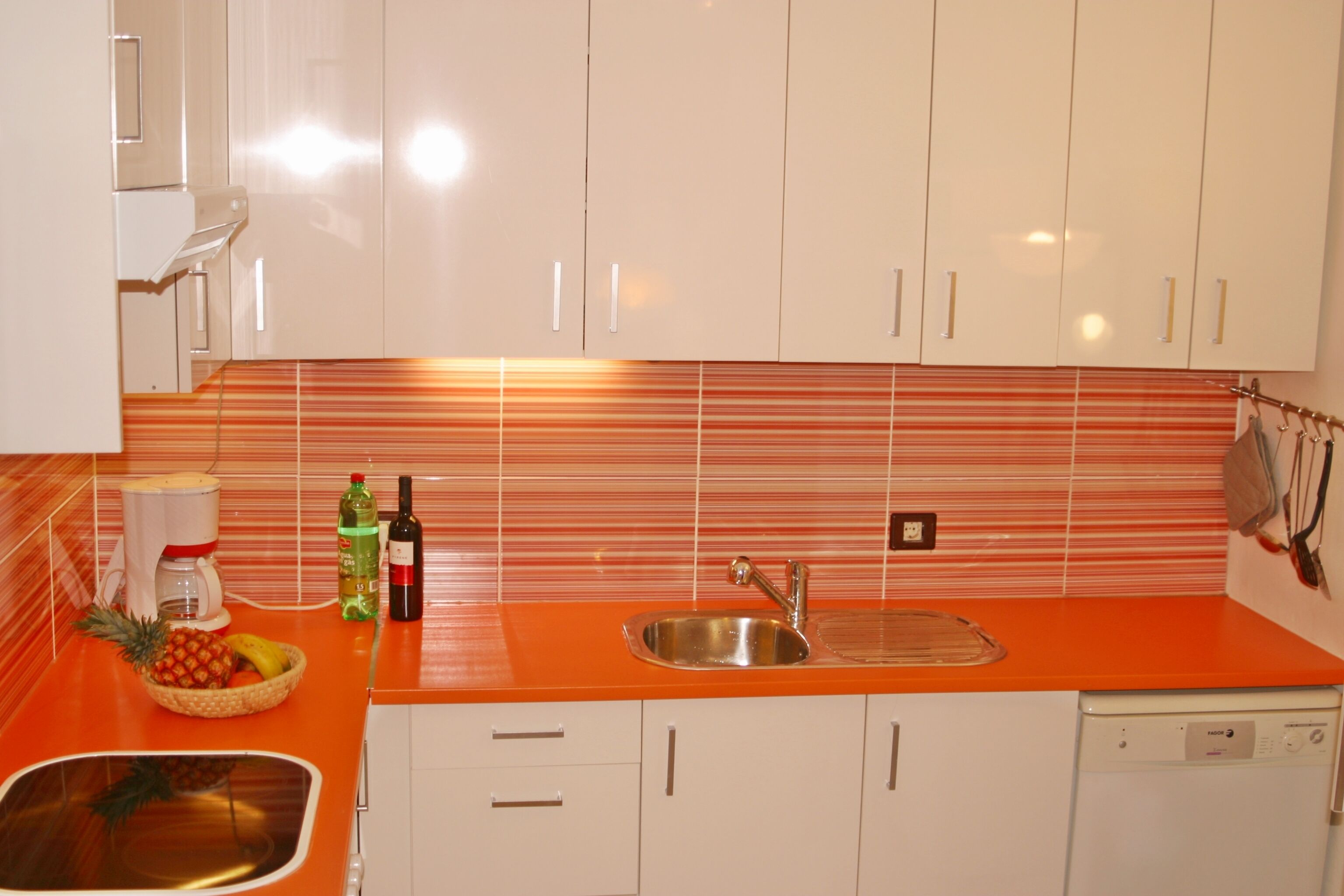Una cocina con gabinetes blancos, una encimera anaranjada, un fregadero de acero inoxidable y un lavavajillas.
