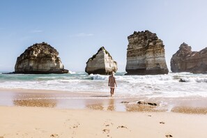 A beach with large rock formations in the background and a person walking on the sand. - Apartments 521 (Warrnambool)