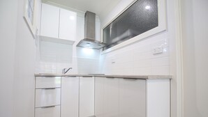 A compact kitchen with white cabinetry, a stainless steel range hood, and a window above the sink. - Apartments 521 (Warrnambool)