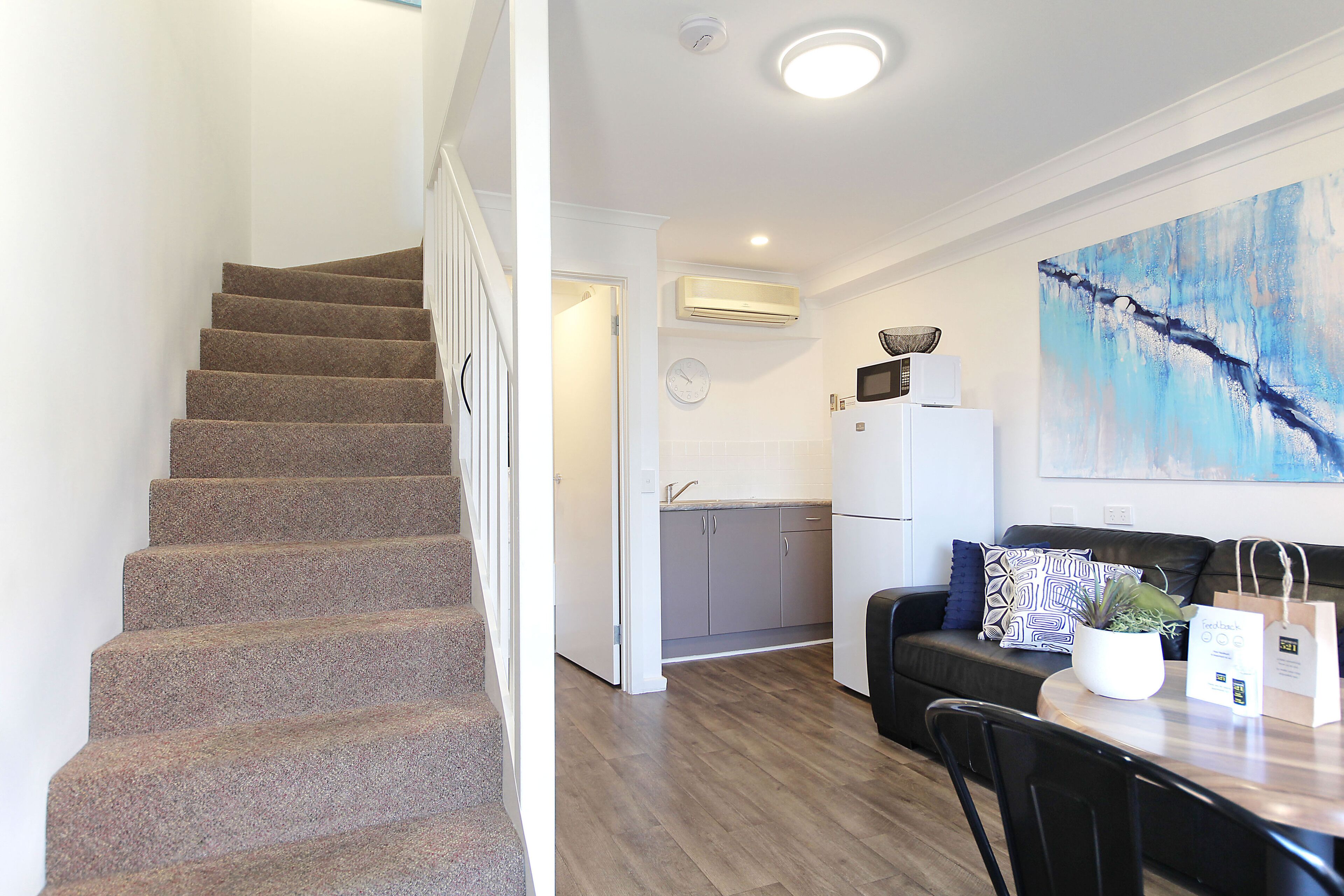 Una escalera conduce a una cocina con microondas, un lavabo y una zona de comedor con mesa y sillas.