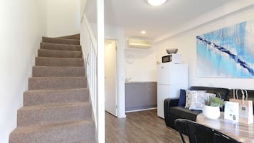 Una escalera conduce a una cocina con microondas, un lavabo y una zona de comedor con mesa y sillas.