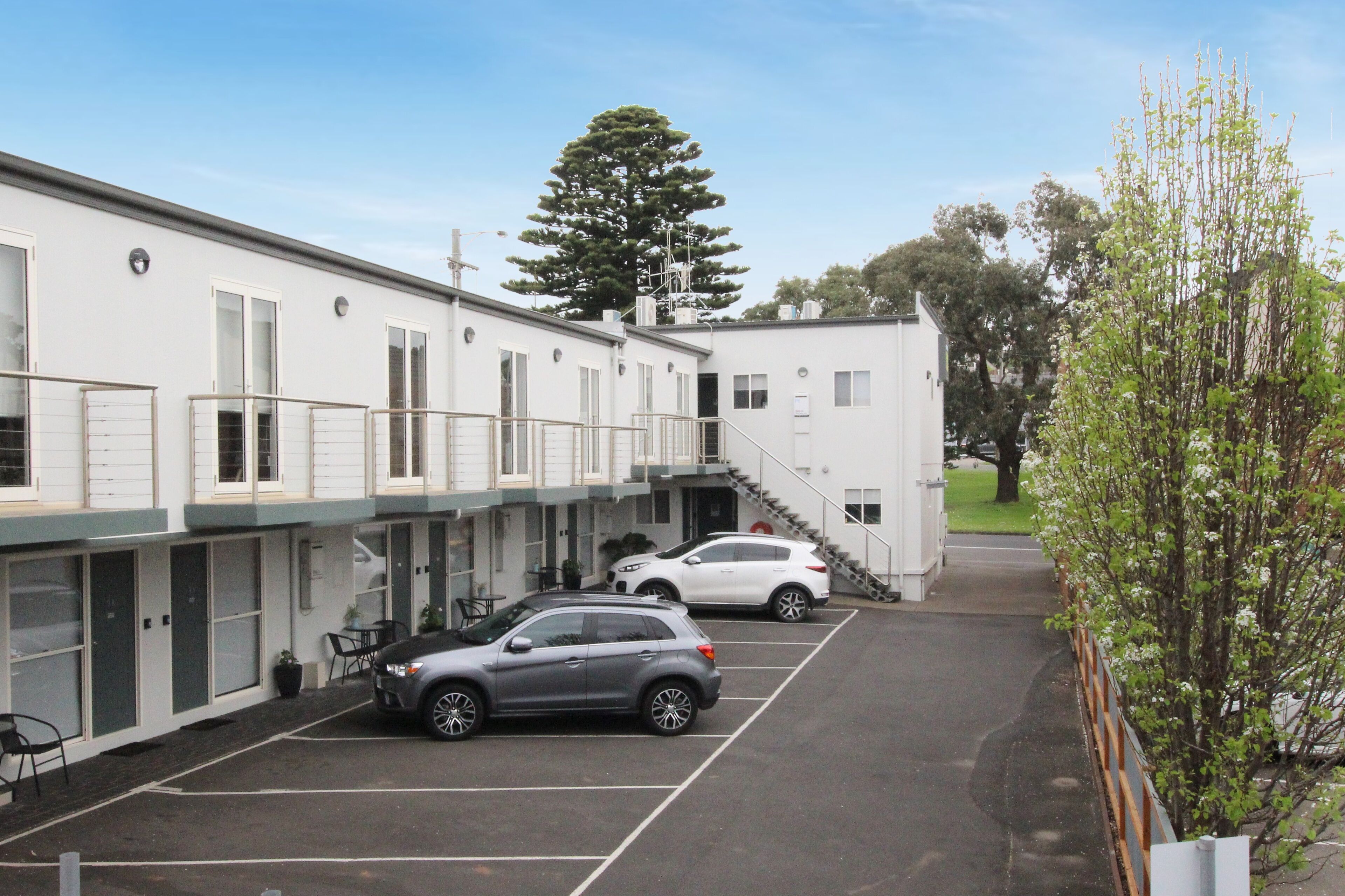 A building with a parking lot, two cars, and a staircase leading to an upper level.