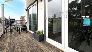 An outdoor patio with a wooden deck, a table with chairs, and a planter with greenery. - Apartments 521 (Warrnambool)