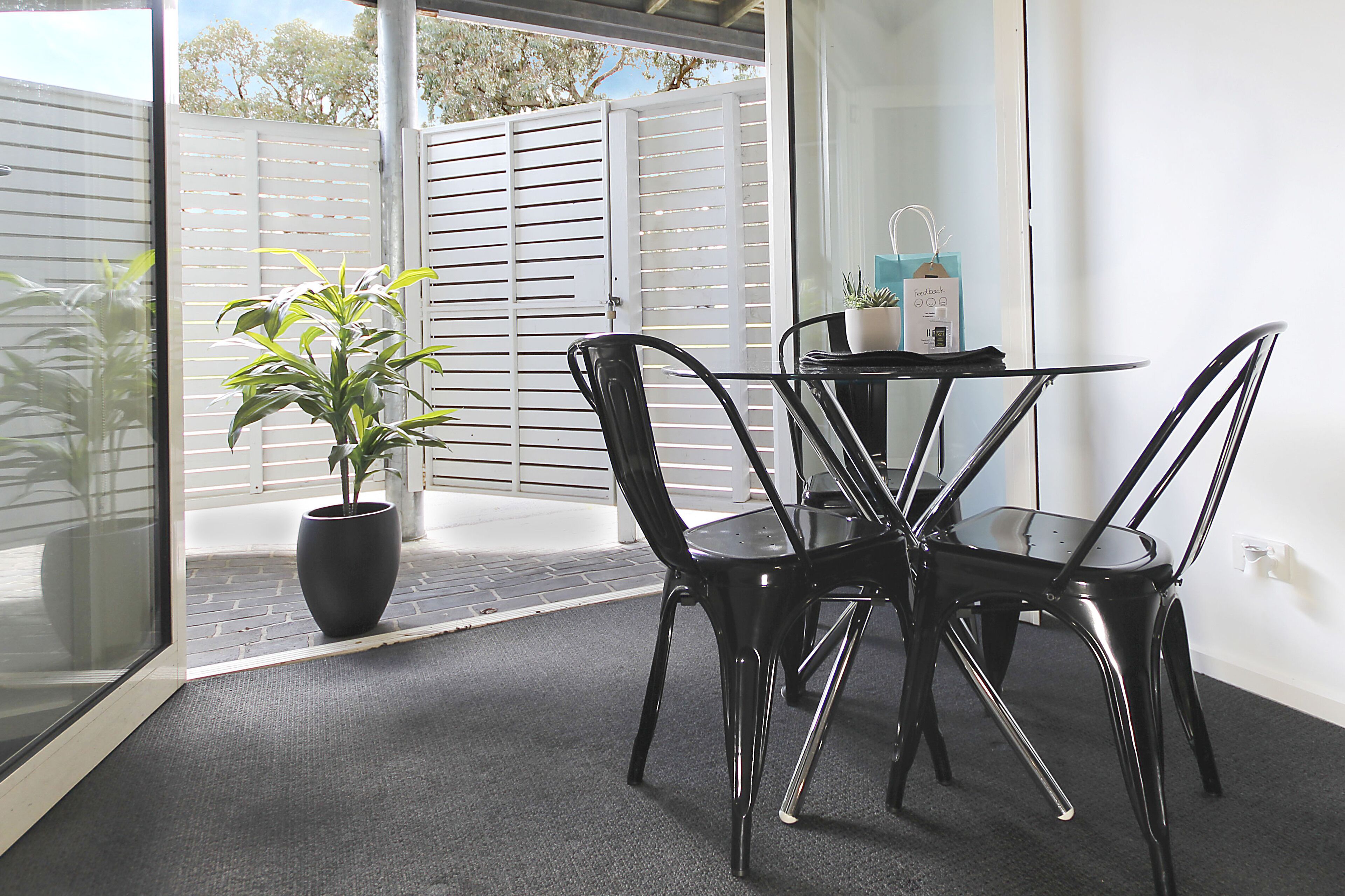A small patio area with a table and chairs, a potted plant, and a white fence.