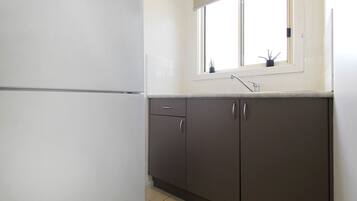A kitchen with a white refrigerator, dark cabinets, a window with a plant, and a sink.