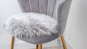 Une chaise dotée d’un siège moelleux et d’un dossier rembourré de couleur grise, soutenue par des pieds dorés, placée devant un mur blanc et sur un plancher en bois.