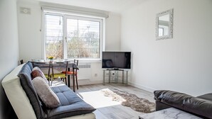 Un salon moderne comprenant un canapé, un téléviseur et un coin repas avec des chaises et une table.