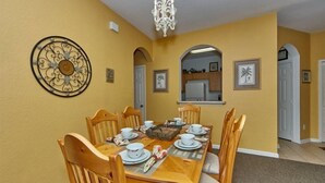 A dining room with a wooden table set for six, surrounded by six wooden chairs with cushioned seats. - Windsor_palms_105_sp (Kissimmee)