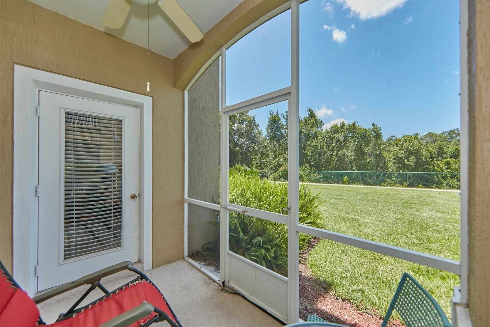 A covered patio with a sliding glass door, a red chair, and a green chair.
