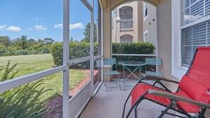 A balcony with a glass door, a small table with chairs, and a red chair. - Windsor_palms_105_sp (Kissimmee)