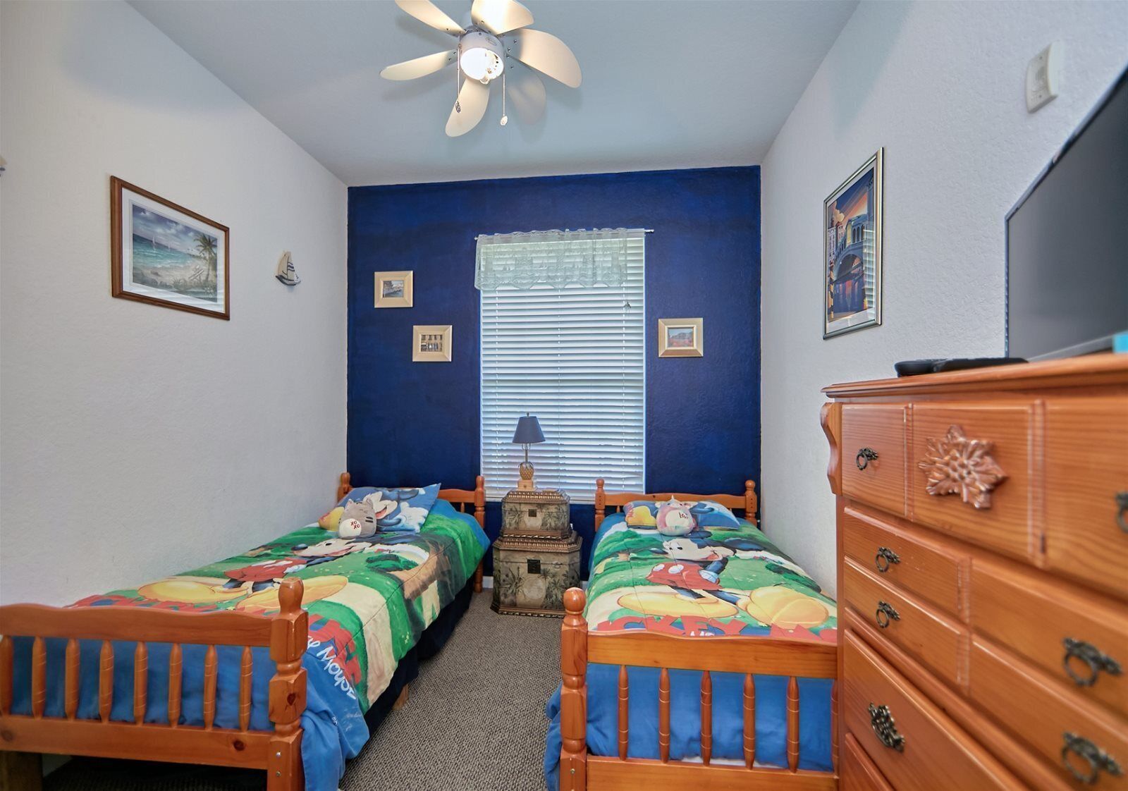 Une chambre avec deux lits en bois, un ventilateur de plafond, une commode et une fenêtre avec des stores.