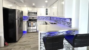 A modern kitchen with white cabinets, a black refrigerator, stainless steel appliances, and a blue-lit backsplash. - Oceanfront 2BR Condo Ilikai 1822 – Steps to Waikiki Beach | Sleeps 6 | Stunning Views (Waikiki)